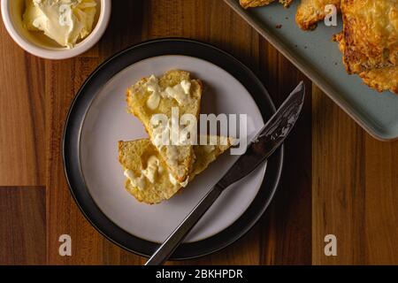 Ein Käse Scone von oben nach unten mit Butter auf dem Scone schmelzen gesehen. Um den Teller eine Schüssel mit Butter und einem Stapel von mehr Käse Scones Stockfoto