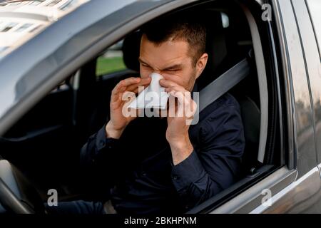 Junger Mann mit Taschentuch. Kranker Kerl hat laufende Nase. Männlich Modell macht ein Heilmittel für die gemeinsame Kälte im Auto. Stockfoto