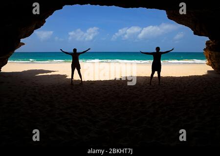 Zwei Touristen silhouetted am Eingang der Meereshöhle am Praia de Santa Mónica, Sandstrand auf der Insel Boa Vista, Kap Verde / Cabo Verde Stockfoto