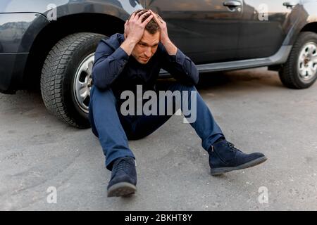 Autounfall, Verkehrsunfall, ein Mann in Verzweiflung sitzt in der Nähe des Rades seines Autos. Er legte seine Hände auf seinen Kopf. Er fühlt Panik und Wutanfall Stockfoto