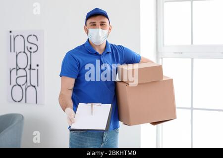 Männlicher Kurier in medizinischer Maske und mit Kisten im Innenbereich Stockfoto