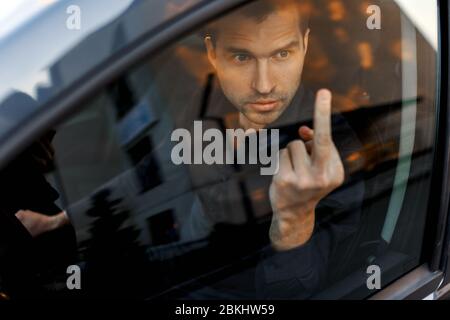 Mann fährt Auto und zeigt Handzeichen mit Mittelfinger