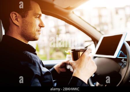 Der Fahrer sieht während der Mittagspause Filme oder Fernsehsendungen auf dem Tablet. Stoppen für einen Happen zu essen. Mann essen Snack im Auto und trinkt Kaffee oder Tee. Stockfoto