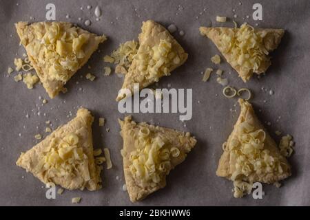 Ein Blick auf rohe Käseschaufeln von oben nach unten. Die Scones wurden in Dreiecke geschnitten und mit geriebenem Käse überstanzt Stockfoto