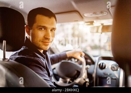 Ein Mann sitzt in einem Autoinnenraum und schaut auf die Kamera und lächelt. Transportkonzept. Stockfoto