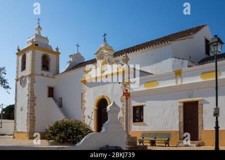 Seite von Igreja Matriz de Alvor - Kirche in einer portugiesischen Stadt. Weiße Fassade mit gelben Details. Strahlend blauer Himmel. Alvor, Algarve, Portugal.