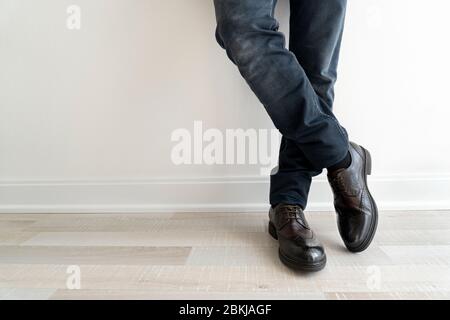 Junger Mann in schwarzen Jeans und zeigt seine neuen braunen Schuhe in der Nähe der Wand bleiben Stockfoto