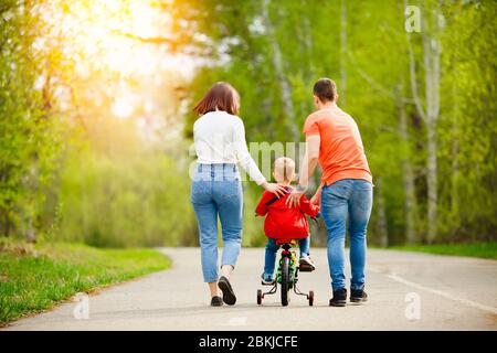 Papa und Mama lehrt kleinen Sohn Fahrrad im Park fahren, Spaß haben Familie, Rückansicht. Stockfoto