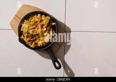 Draufsicht von geschmorten Kohl und Zucchini in Gusseisen Pfanne auf Keramikfliesen Hintergrund mit harten Schatten Stockfoto