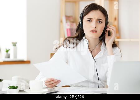 Ernst gut gekleidete Verkäuferin am Telefon sprechen im Büro hinter ihrem Schreibtisch und Laptop. Platz kopieren Stockfoto