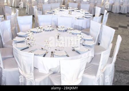 Runde Tische mit weißer Tischdecke und Stühle mit weißer Abdeckung. Alles ist für ein Bankett vorbereitet Stockfoto