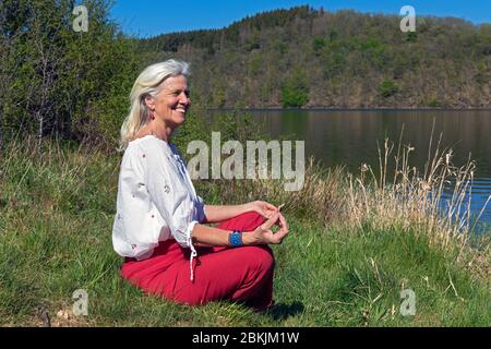 Europa, Luxemburg, Insenborn, attraktive ältere Frau glücklich meditierend von Lac Sûre Stockfoto