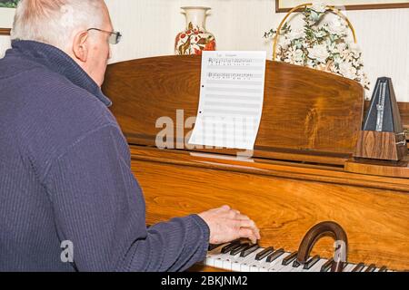 Älterer Mann sitzt am Klavier und Spazierstock, der erste Klavierstunde hat. Konzept: Altersaktivität, Stimulation, Lernen, nie zu alt, jung halten. Stockfoto