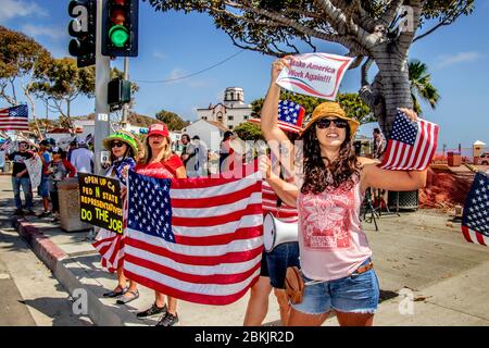 Multirassische Demonstranten, die sich gegen die landesweite Lockdown-Order des kalifornischen Gouverneurs Gavin Newsom zur Bekämpfung der COVID-19-Pandemie am Pacific Coast Highway in Laguna Beach, CA, erheben, die eine patriotische Pose beeinflussen. Stockfoto