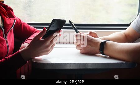 Mann und Frau mit Telefonen in den Händen sitzen im gleichen Fach des Zuges, konzentrieren sich auf männliche Hände mit Smartphone Stockfoto