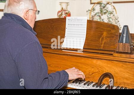 Älterer Mann sitzt am Klavier und Spazierstock, der erste Klavierstunde hat. Konzept: Altersaktivität, Stimulation, Lernen, nie zu alt, jung halten. Stockfoto