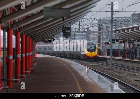 Virgin Trains Alstom der Klasse 390 Pendolino Zug vorbei Rugby Bahnhof im Regen mit dem Bahnhof Baldachin. Stockfoto