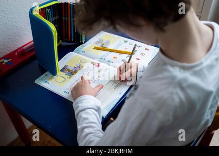 Erstklaessler (7 Jahre) sitzt zu Hause an einem Tisch und erledigt deutsche Aufgaben in seinem Booklet "Alphabet Booklet - BASIC Font", am 4. Mai 2020 in Mülheim an der Ruhr. ¬ Verwendung weltweit Stockfoto