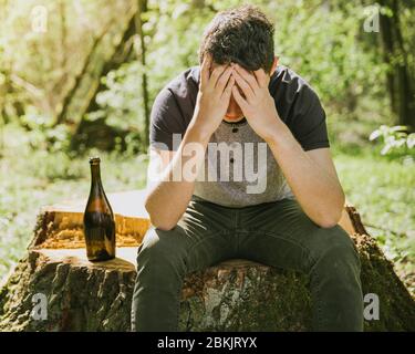 Ein unglücklicher Mann löst Probleme mit Alkohol. Traurig und allein mit einer Flasche Alkohol in der Natur Stockfoto