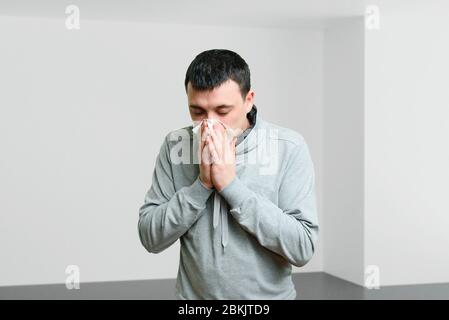 Сold junger Mann wischt seine Nase mit einem Taschentuch ab. Symptome von saisonalen Allergien Stockfoto