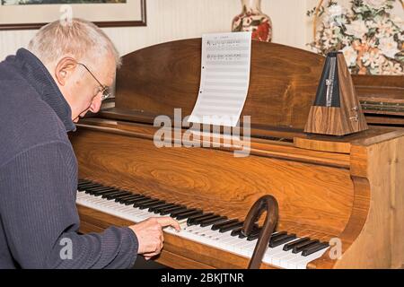 Älterer Mann sitzt am Klavier und Spazierstock, der erste Klavierstunde hat. Konzept: Altersaktivität, Stimulation, Lernen, nie zu alt, jung halten. Stockfoto