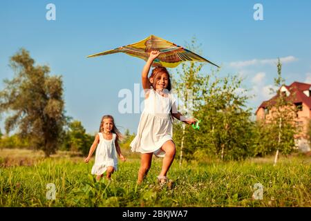 Glückliche kleine Mädchen mit Kite-Running auf der Wiese im Frühlingspark. Kinder, die Spaß haben, draußen zu spielen Stockfoto