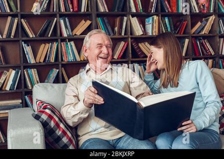 Vater und Tochter zu Hause Bibliothek sitzen halten Album lachen über Bilder Stockfoto