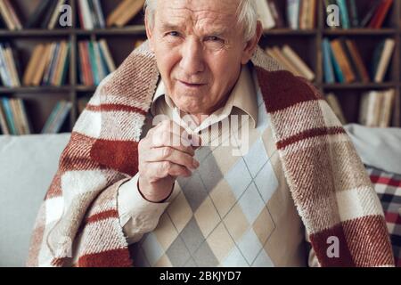 Der ältere Mann allein sitzt in der Bibliothek und ist mit karierten Kamerahusten bedeckt Stockfoto