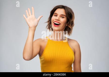 Glücklich lächelnde junge Frau winkende Hand Stockfoto