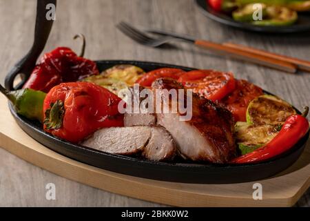 Nahaufnahme von gegrilltem Fleisch auf gusseisernen Pfanne mit gegrilltem Gemüse auf rustikalen Holztisch. Stockfoto