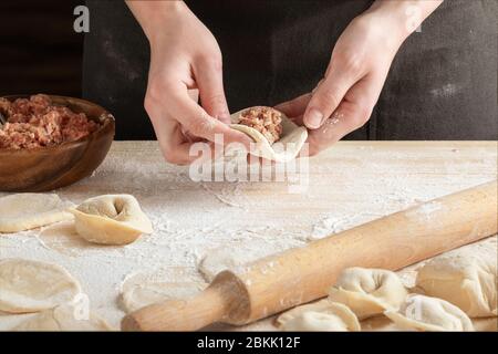 Vorderansicht der Hände der Frau, die Fleischknödel mit Holz-Nudelholz machen. Stockfoto