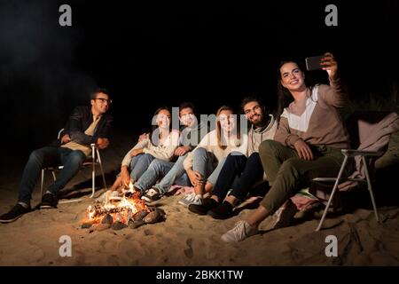 Glückliche Freunde, die Selfie am Lagerfeuer am Strand machen Stockfoto