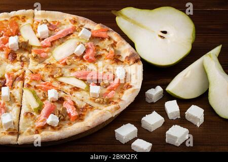 Pizza mit Lachs, Feta, Walnüssen und Birne auf Holzhintergrund. Stockfoto