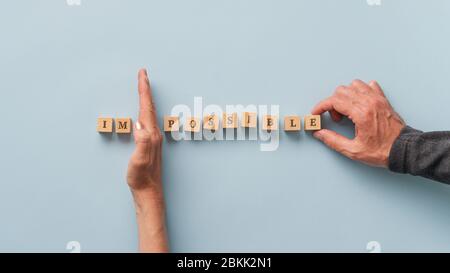 Männliche und weibliche Hände ändern das Wort unmöglich zu möglich geschrieben auf Holzblöcken. Über blauem Hintergrund. Stockfoto