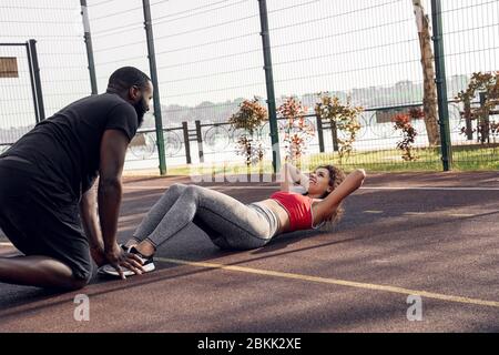 Outdoor-Aktivitäten. African paar stehend auf Basketball Gericht Kerl helfen Mädchen tun knirscht lächelnd fröhlich Stockfoto