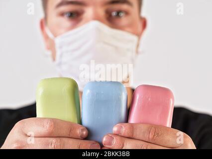 Junger Mann mit Gesicht Virus Nase Mund Maske mit bunten Seifenstücke, Fokus auf Seifen, verschwommenes Gesicht im Hintergrund. Coronoavirus covid-19 Ausbruch prev Stockfoto