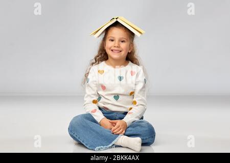 Portrait von lächelndes Mädchen mit Buch auf dem Kopf Stockfoto