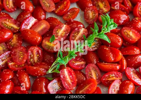 Rohe Traubentomaten auf einer Sheet Pan: Halbierte Traubentomaten und ein Zweig frischen Oregano, gewürzt mit Salz, Pfeffer und Olivenöl Stockfoto