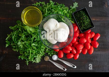 Rucola mit langsam gerösteten Tomaten und Burrata: Zutaten für eine andere Art des klassischen Caprese-Salats aus Traubentomaten, Rucola, Basilikum Stockfoto