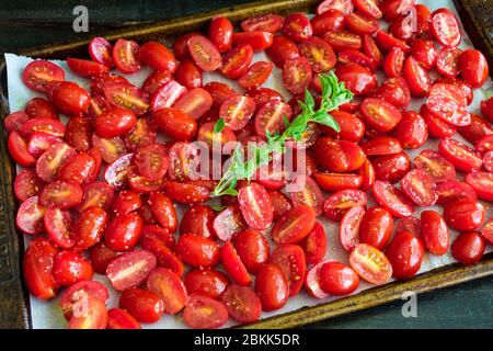 Rohe Traubentomaten auf einer Sheet Pan: Halbierte Traubentomaten und ein Zweig frischen Oregano, gewürzt mit Salz, Pfeffer und Olivenöl Stockfoto