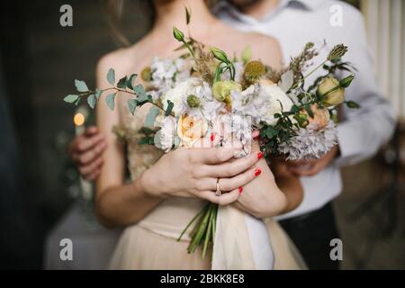 Der Bräutigam umarmt die Braut und hält in den Händen einen Brautstrauß Stockfoto