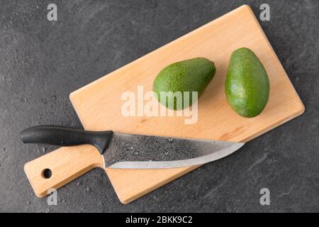 Zwei Avocados und Küchenmesser auf Schneidebrett Stockfoto