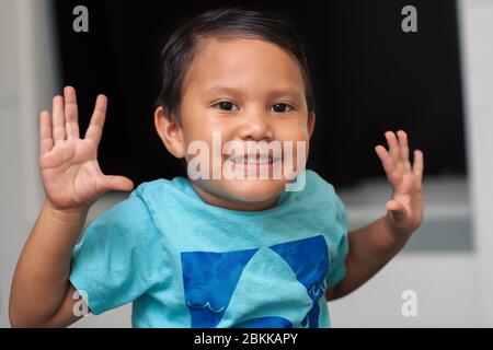 Junger Junge, der seine Hände und Finger benutzt, während er zählt, das Alter eines Vorschulalters und beide Hände hoch hebt, während er lächelt. Stockfoto