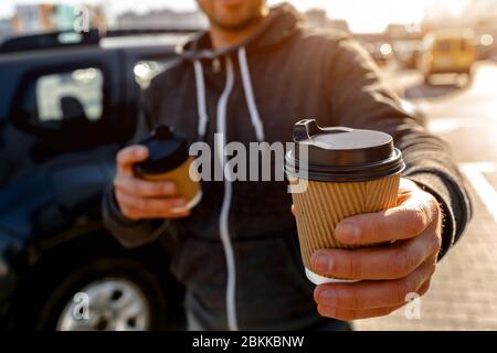 Einweg-Pappbecher mit Heißgetränk. Ein Mann trinkt Kaffee oder Tee und bietet an, einen Drink mit Ihnen zu teilen Stockfoto