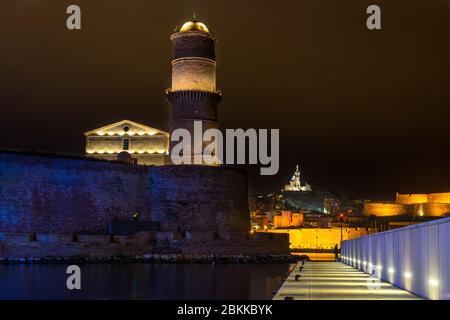 Nachtansicht von Marseille Alter Hafen mit ehemaligen Leuchtturm von Fort Saint-Jean und Notre Dame de la Garde im Hintergrund beleuchtet, Frankreich Stockfoto