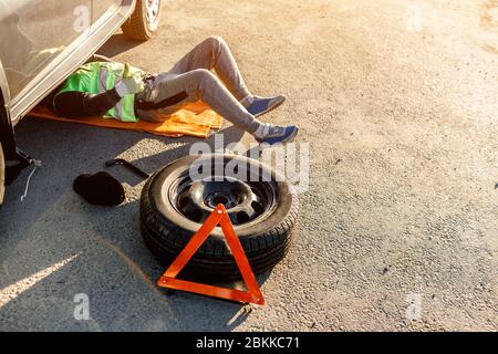Ein Fahrer oder Arbeiter repariert ein defektes Auto auf der Seite der Straße. Blick von oben. Der Mensch steht unter dem Auto Stockfoto