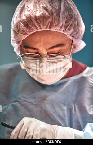 Close up Portrait von jungen weiblichen Chirurg Arzt durch das Tragen von schützender Maske und Hut während der Operation. Gesundheitswesen, medizinische Ausbildung, Chirurgie Konzept Stockfoto