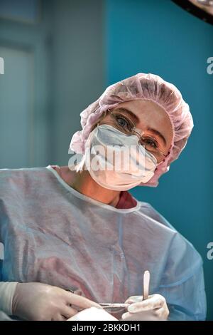 Close up Portrait von jungen weiblichen Chirurg Arzt durch das Tragen von schützender Maske und Hut während der Operation. Gesundheitswesen, medizinische Ausbildung, Chirurgie Konzept Stockfoto