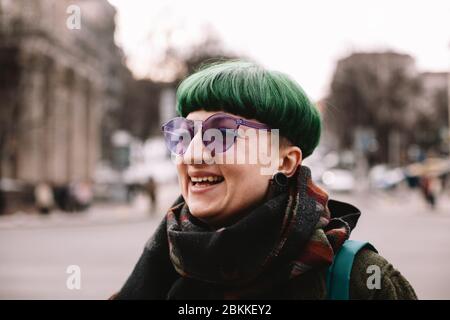 Porträt der glücklichen Punk-Frau in lila Sonnenbrille in der Stadt stehen Stockfoto