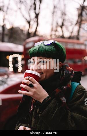 Porträt von glücklichen nicht-binären Hipster Kaffee trinken, während auf der Straße in der Stadt im Winter Stockfoto